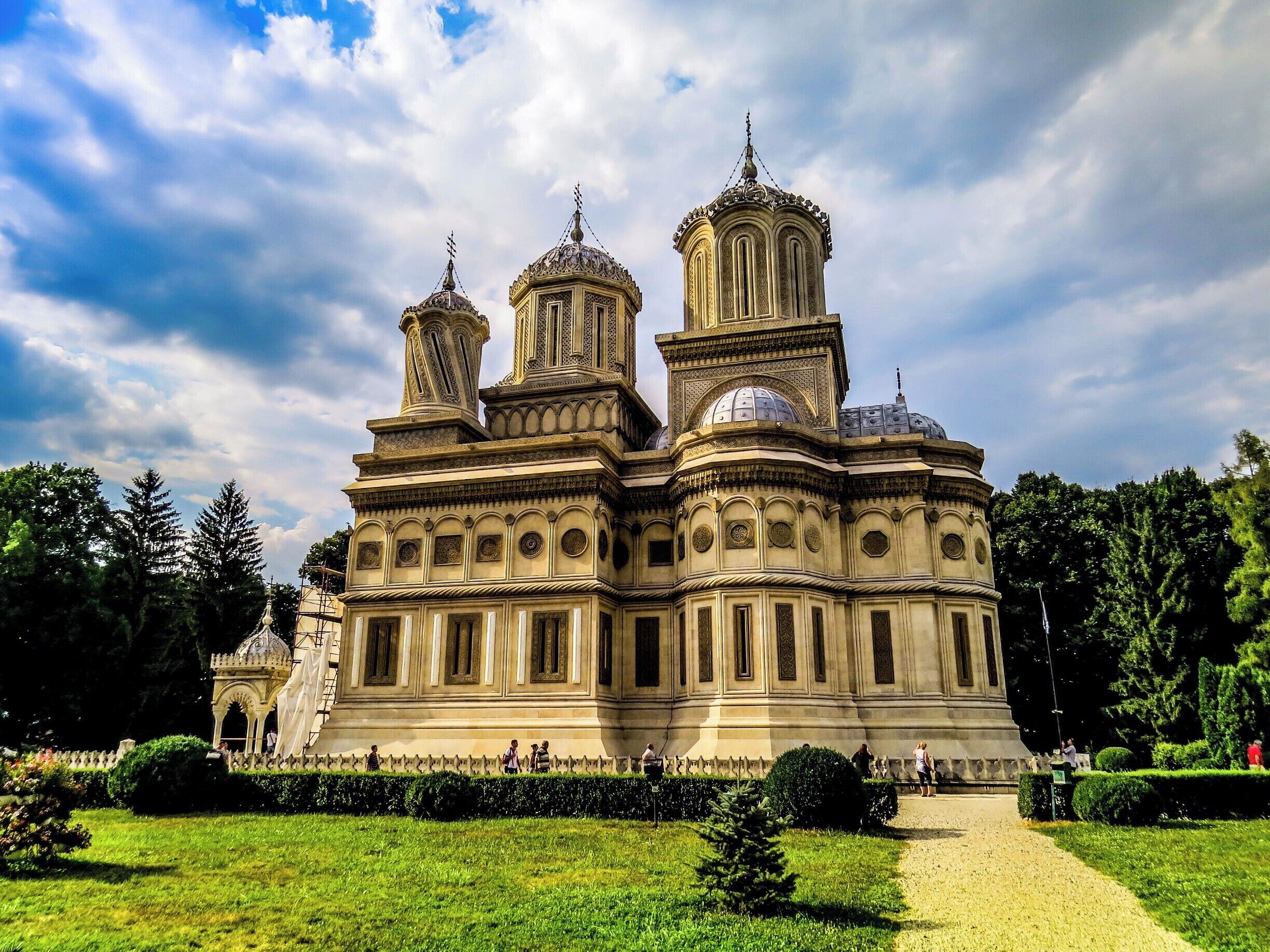A historic building with ornate architecture, surrounded by a well-maintained garden and trees.