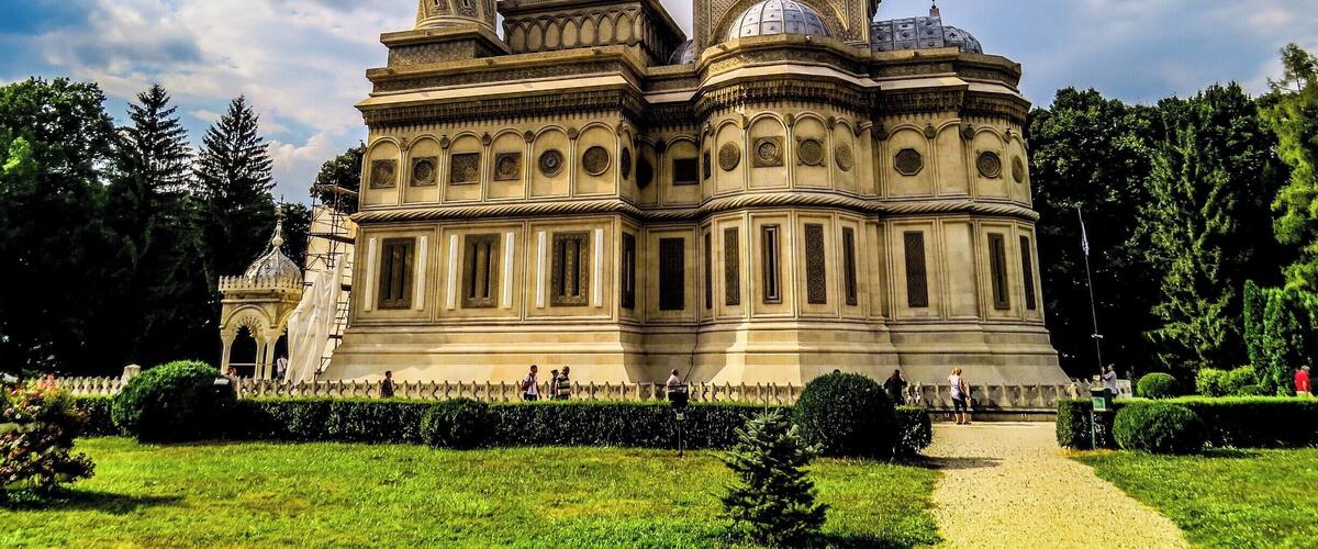 A historic building with ornate architecture, surrounded by a well-maintained garden and trees.