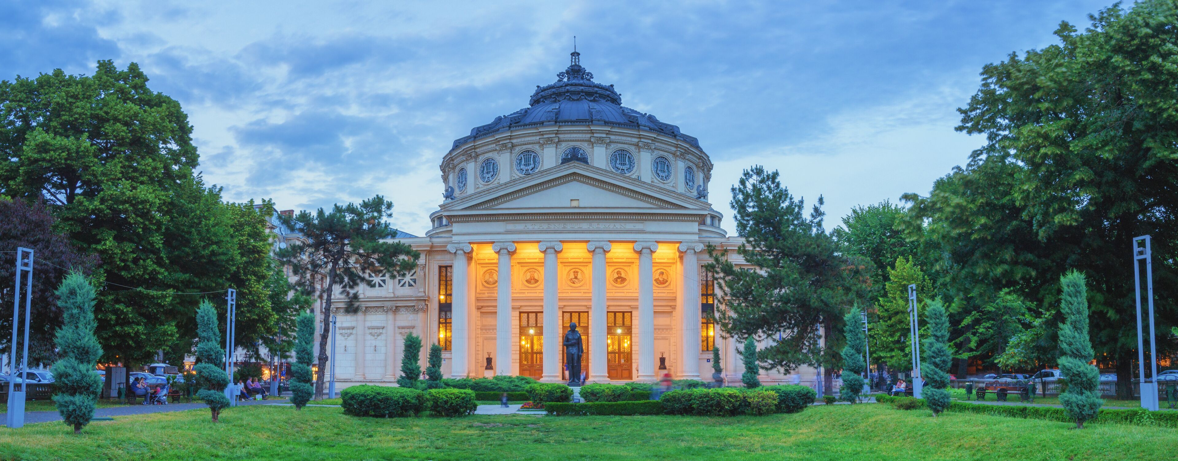 A grand neoclassical building with a dome and columns, surrounded by lush greenery and trees.