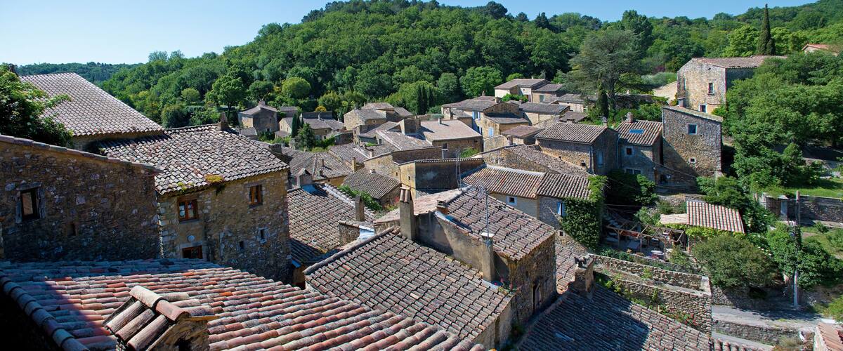 A village with stone buildings and terracotta roofs, surrounded by lush green hills.