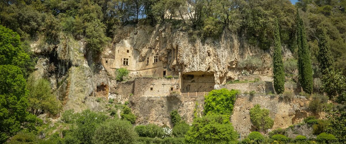 A historic cliffside ruin with ancient buildings carved into the rock, surrounded by lush greenery.