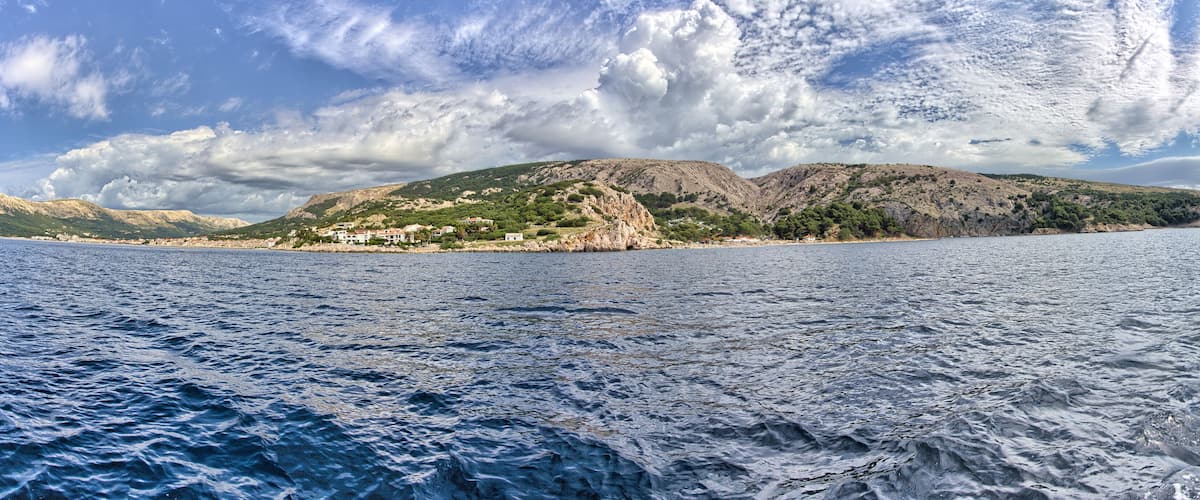 A coastal landscape with a rocky hill, a small settlement, and a body of water.