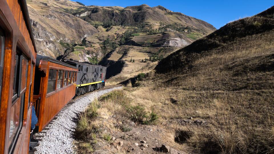 A train on a track through a mountainous landscape with rocky terrain and sparse vegetation.