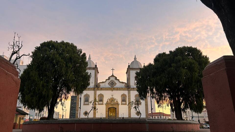 A historic church with two domes and a central entrance, surrounded by trees and a paved plaza.