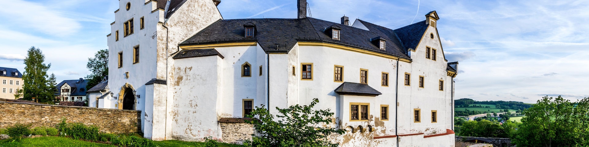 Eine große weiße Burg mit zahlreichen Türmen und einer üppigen, grünen Landschaft darum.