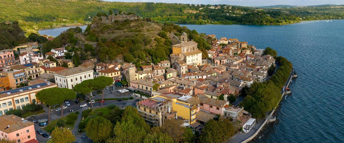 A coastal town with historic architecture, a prominent castle on a hill, and a calm lake.