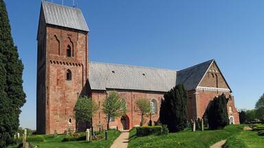 A large brick church with a tall tower and a steeply pitched roof.