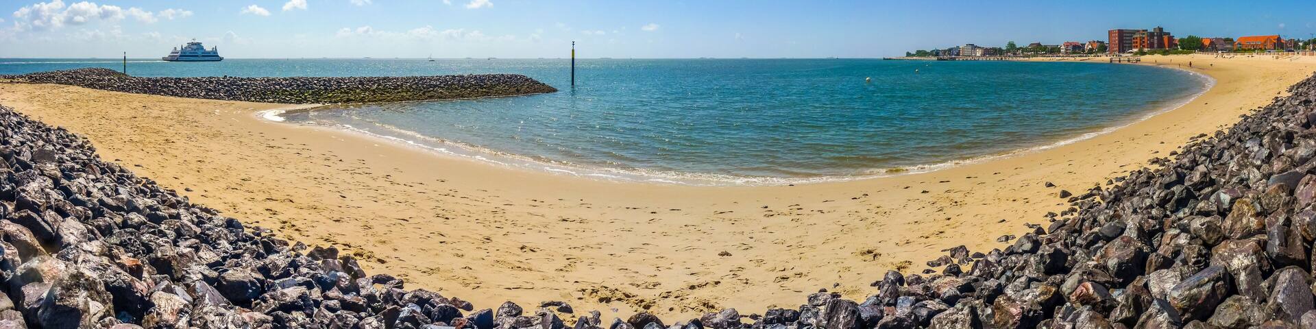 A sandy beach with a rocky breakwater, calm sea, and buildings in the background.