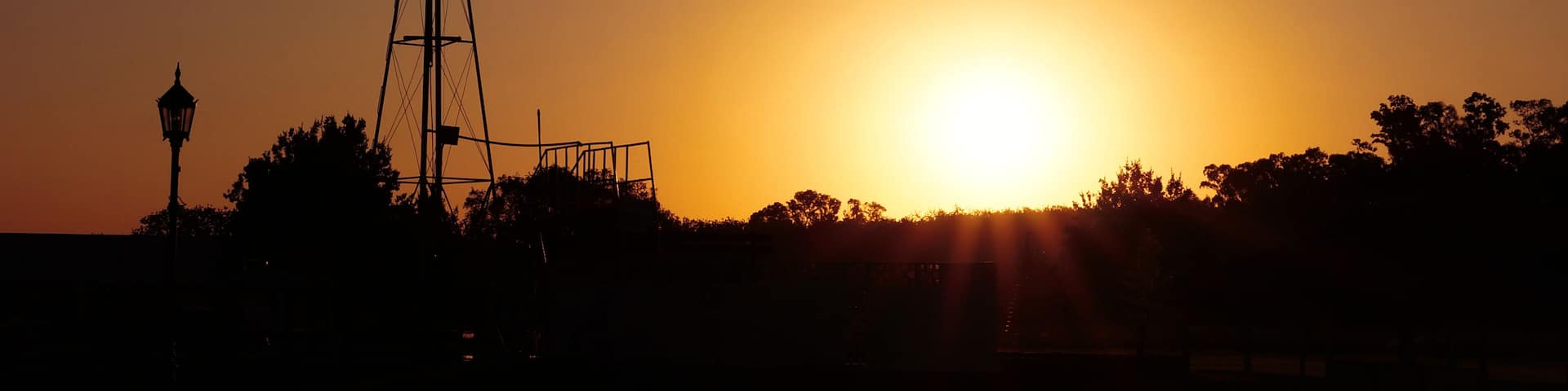 Sunset landscape in countryside. A windmill silhouette in a farm located in Brandsen, BUenos Aires, Argentina. In the background a few small trees and the sun almost hidden. Taken on a warm summer af