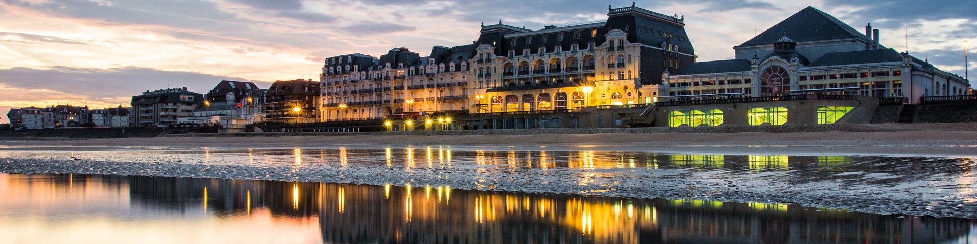Un paisaje marítimo con edificios reflejándose en el agua, un puente y un cielo nublado.