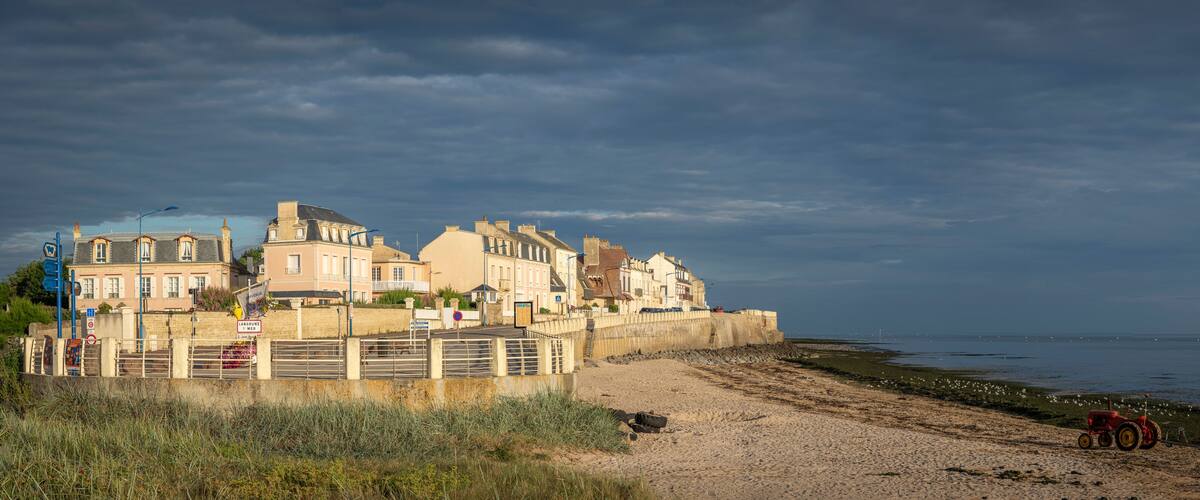 A coastal town with historic buildings, a sandy beach, and a tractor on the shore.