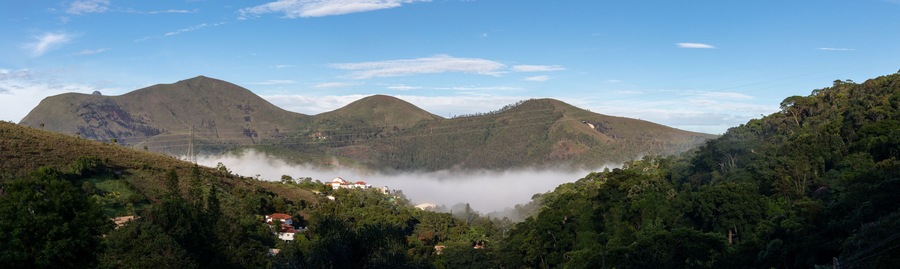 Dawn with low fog in mountain valley, mountainous landscape, view of green countryside with country houses, blue sky, Itaipava, Rio de Janeiro, Brazil