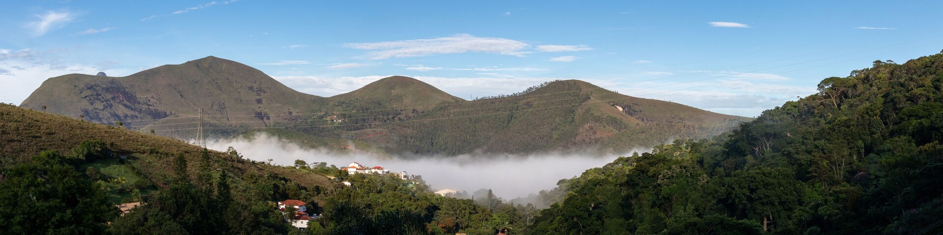 Dawn with low fog in mountain valley, mountainous landscape, view of green countryside with country houses, blue sky, Itaipava, Rio de Janeiro, Brazil