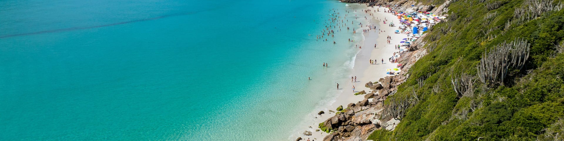 A turquoise beach with clear waters, a rocky shoreline, and lush green hills in the background.