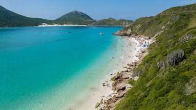 Uma praia turquesa com águas cristalinas, um litoral rochoso e colinas verdejantes ao fundo.