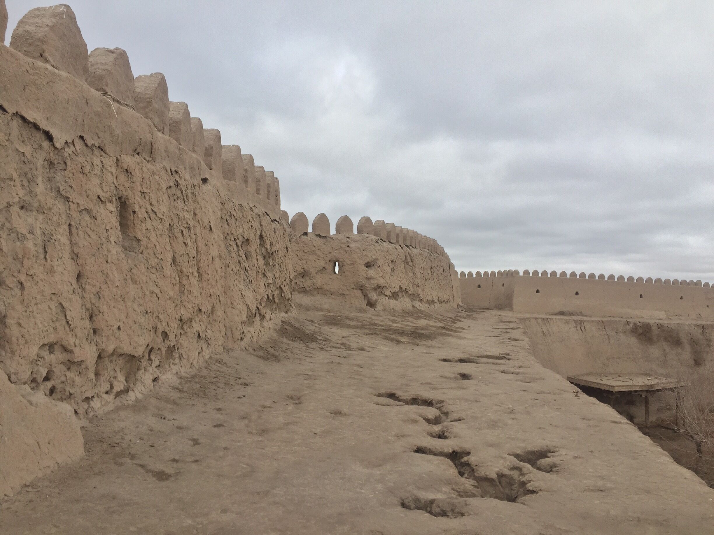 A long, straight pathway flanked by high, earthen walls with crenellations.