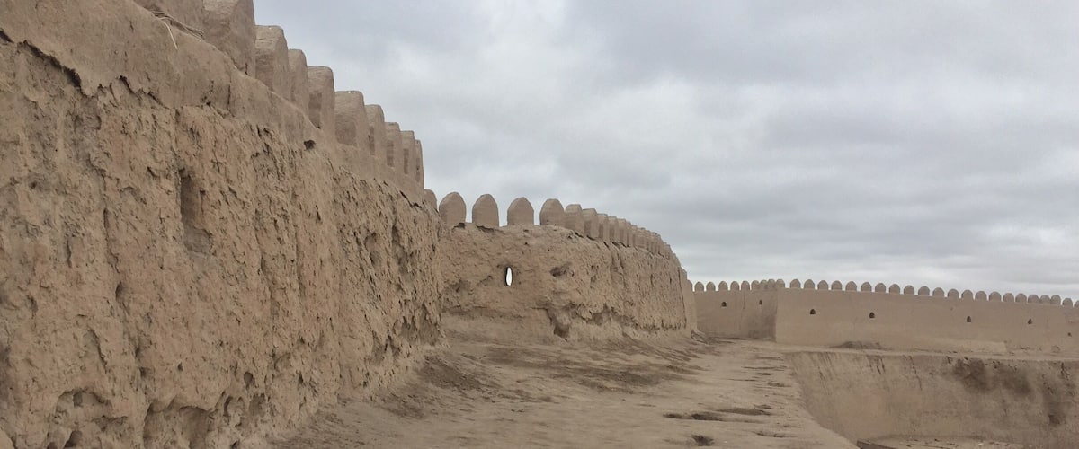 A long, straight pathway flanked by high, earthen walls with crenellations.