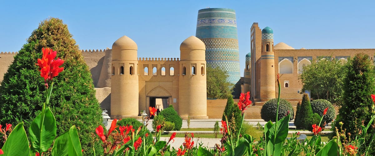 A historic building with two prominent towers, a tall minaret with intricate patterns, and lush greenery in the foreground.