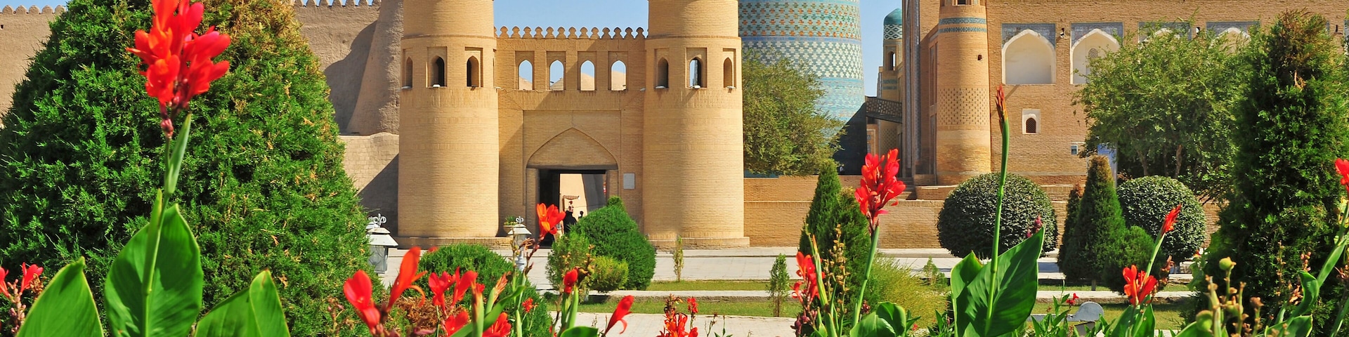 A historic building with two prominent towers, a tall minaret with intricate patterns, and lush greenery in the foreground.