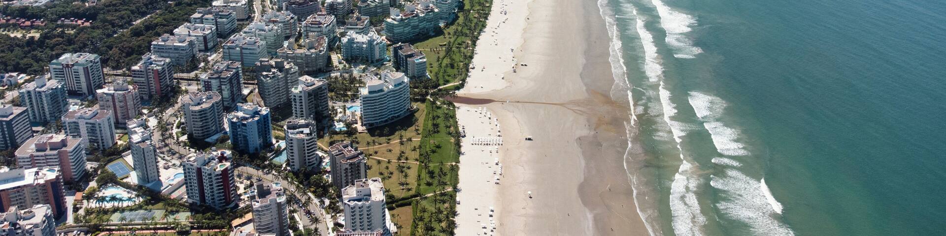 An aerial view of a coastal city with a long beach, dense urban area, and a mountainous island in the distance.