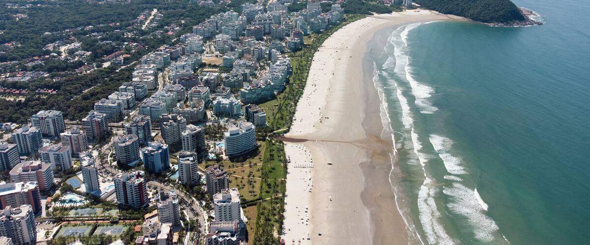 An aerial view of a coastal city with a long beach, dense urban area, and a mountainous island in the distance.