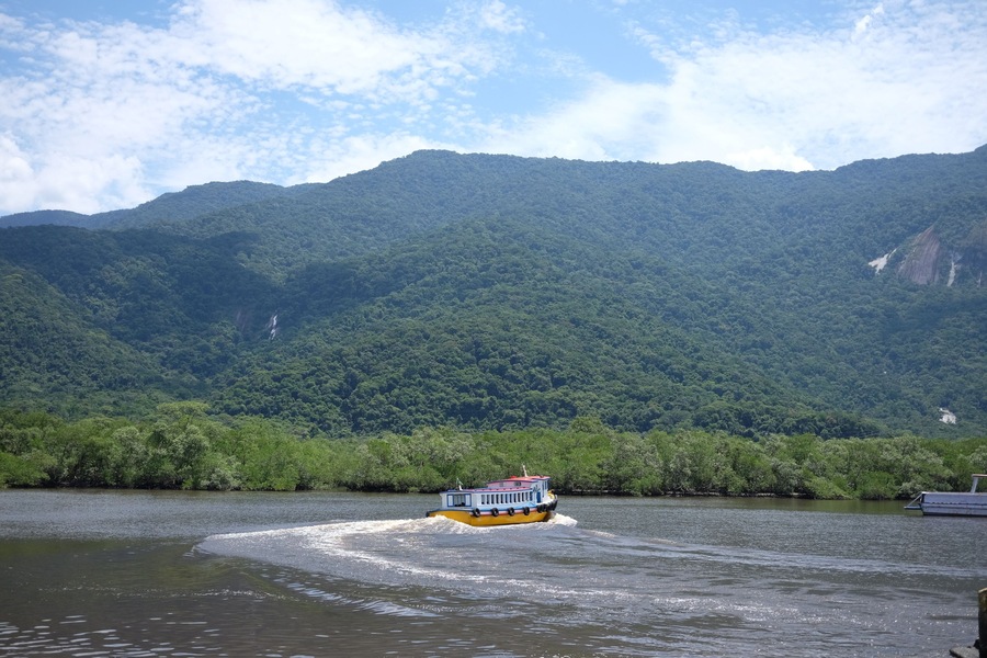 A cruise boat touring the small river close to Bertioga Brazil on a sunny day before the hills with green woods, wild nature life