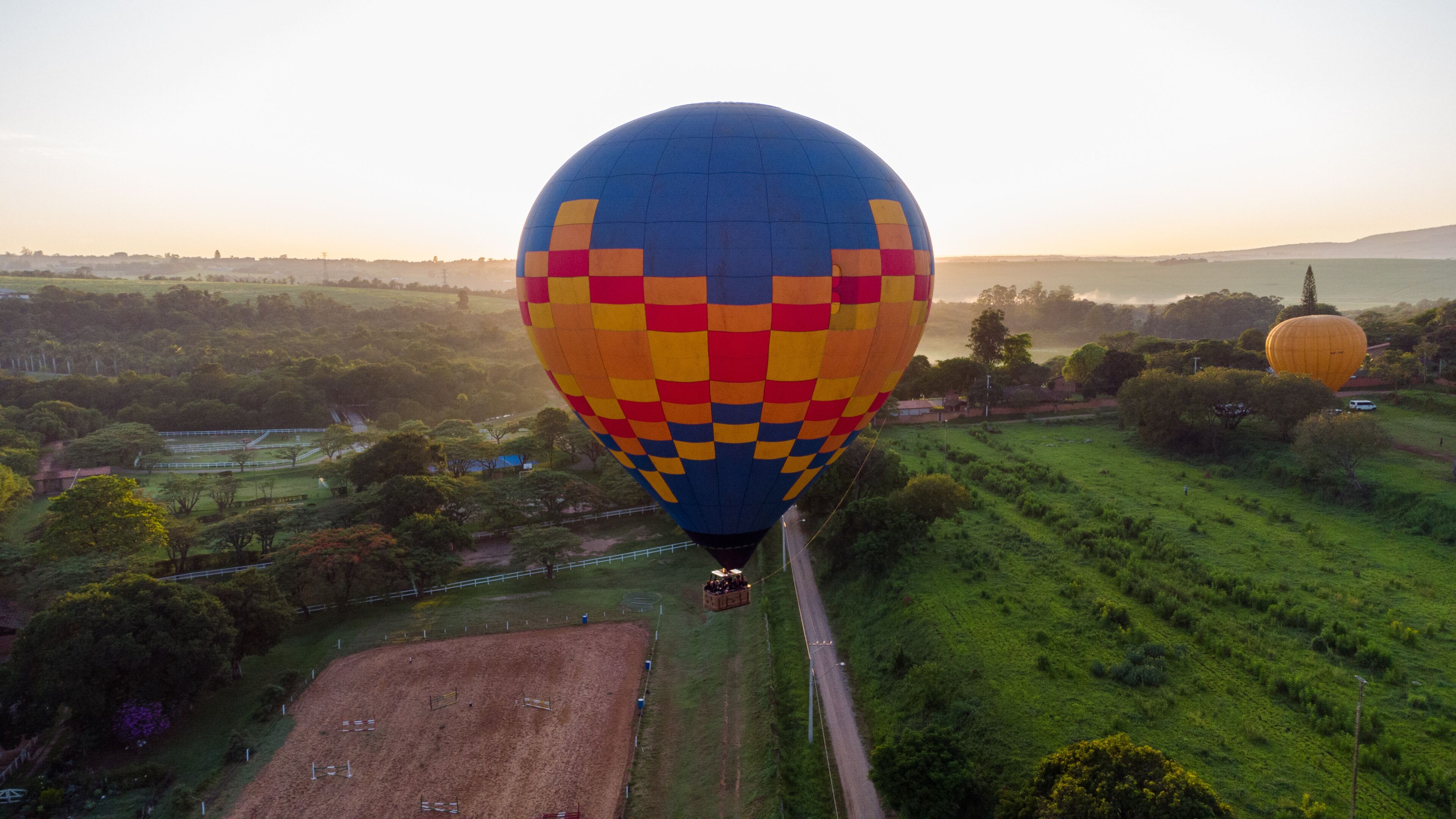 A hot air balloon with a checkered pattern flying over a rural landscape with fields and trees.