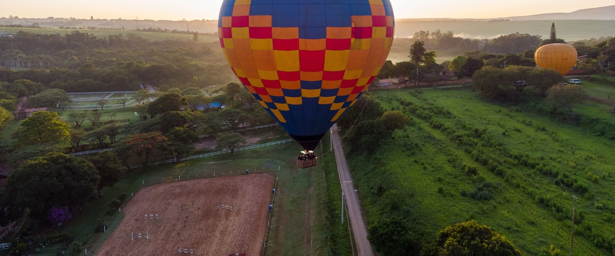 A hot air balloon with a checkered pattern flying over a rural landscape with fields and trees.
