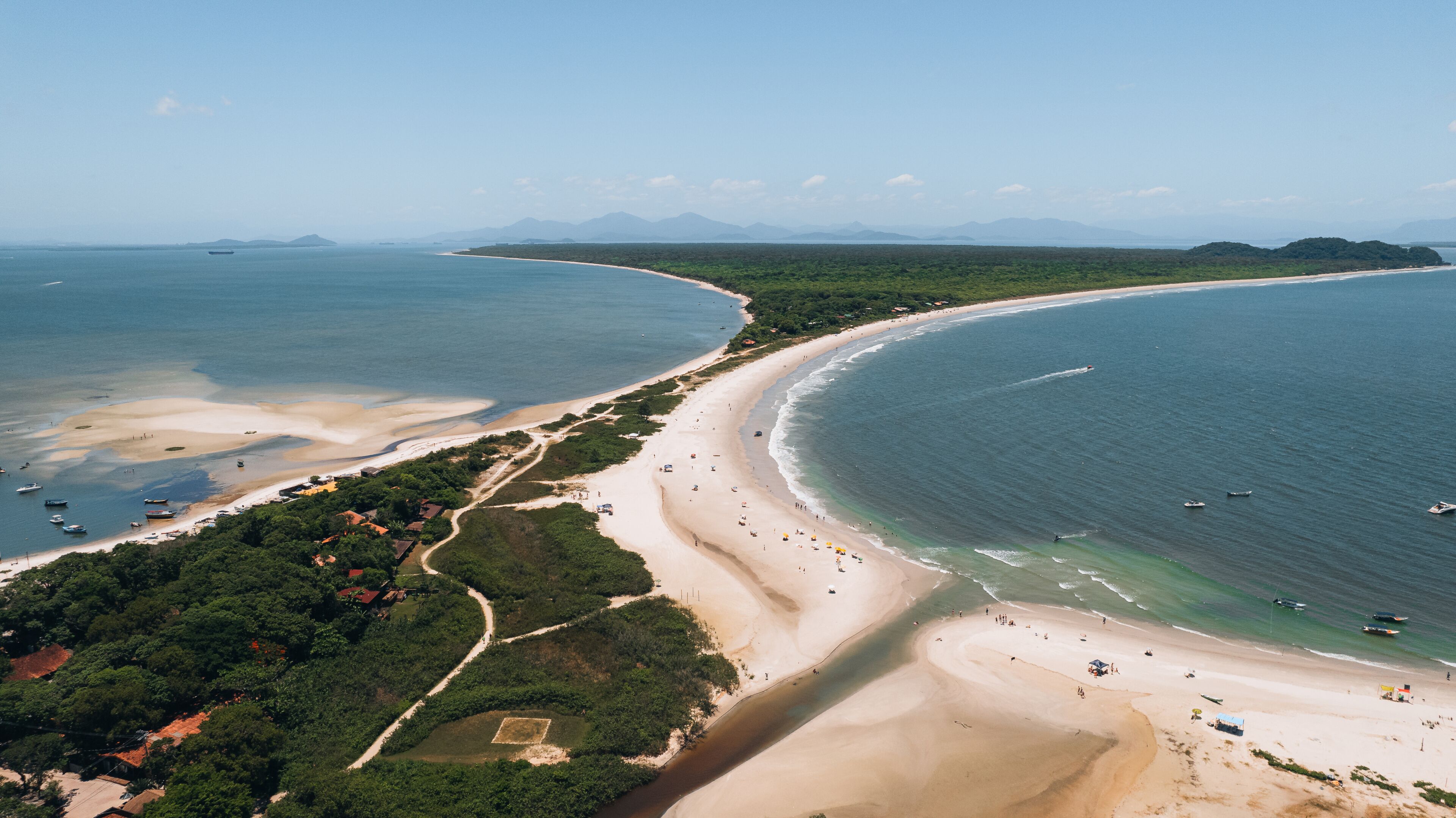 A coastal landscape with a sandy beach, clear blue waters, and distant mountains.
