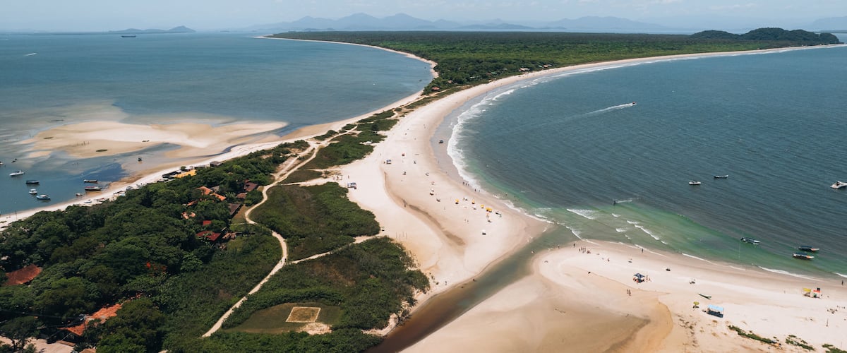 A coastal landscape with a sandy beach, clear blue waters, and distant mountains.
