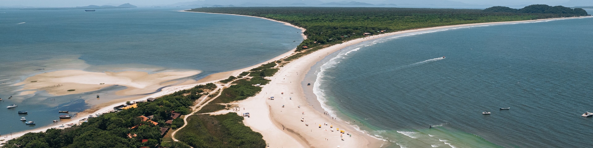 A coastal landscape with a sandy beach, clear blue waters, and distant mountains.