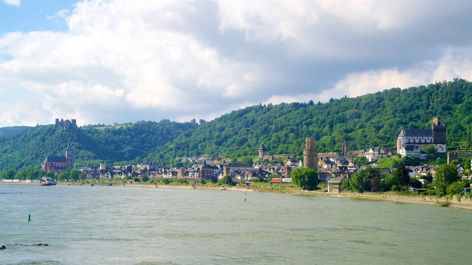 A riverside town with historic buildings, a castle on a hill, and lush green hills.