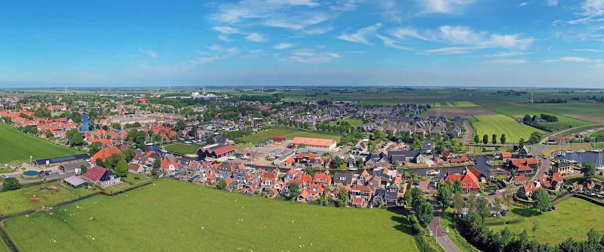 An aerial view of a town with red-roofed houses, green fields, and a river.