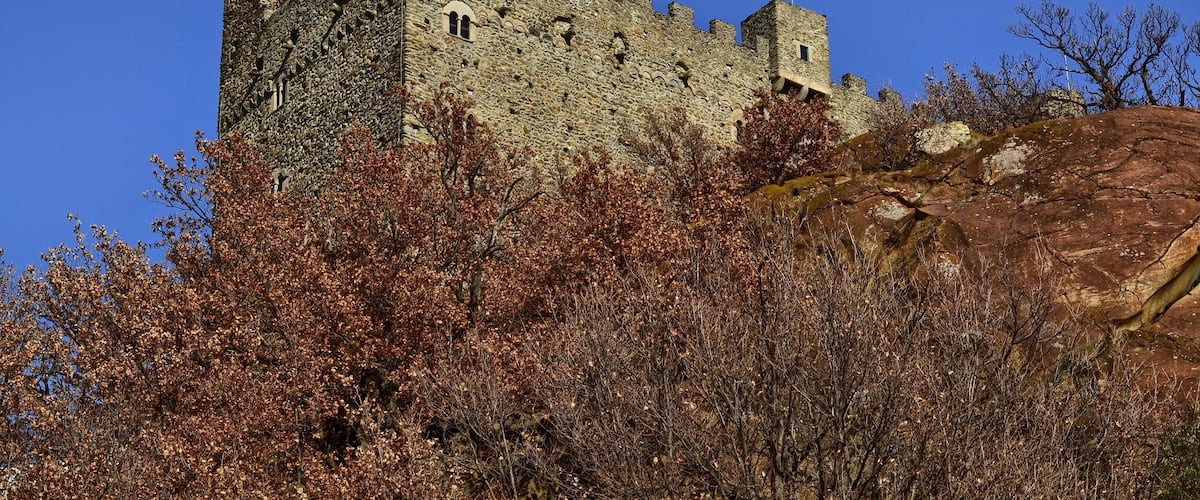 A medieval castle with a round tower, surrounded by autumn foliage.
