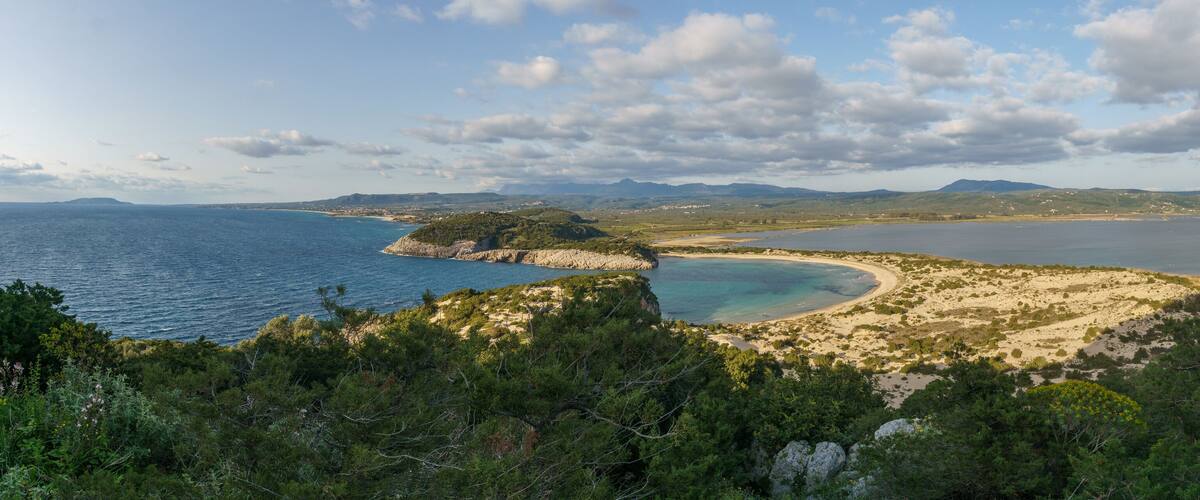 A coastal landscape with a sandy beach, a rocky outcrop, and a clear view of the sea.