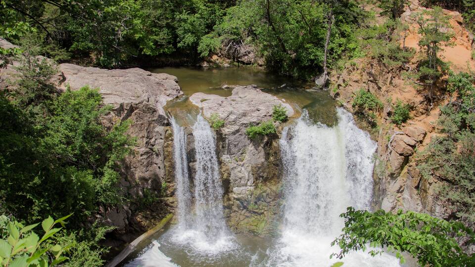 A waterfall cascading down a rocky cliff surrounded by dense green foliage.