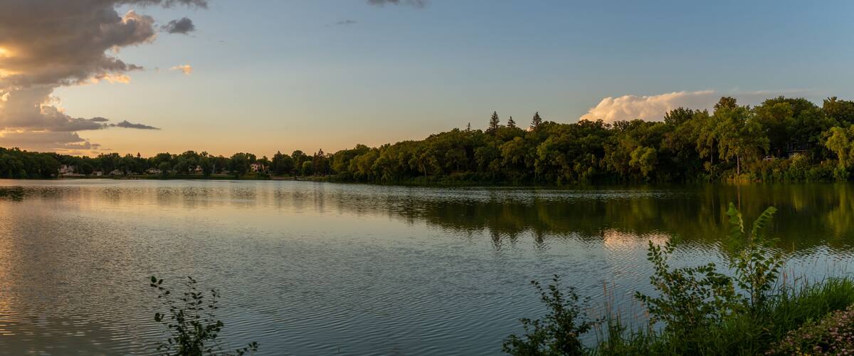 A calm lake with a forested shoreline and a few houses in the background.