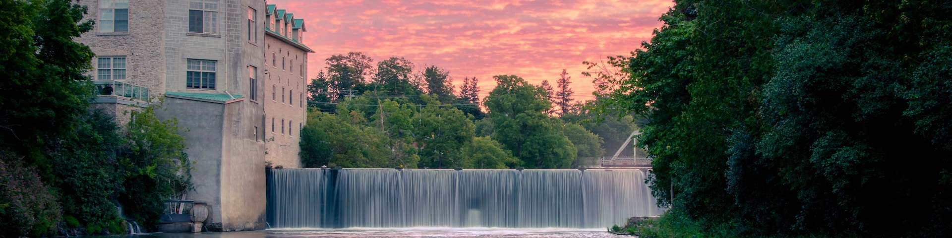Uma cascata, um edifício com telhado verde e um céu ao pôr do sol.