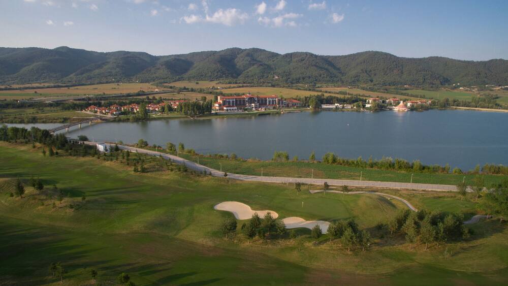 A golf course with a lake, mountains, and residential buildings in the background.