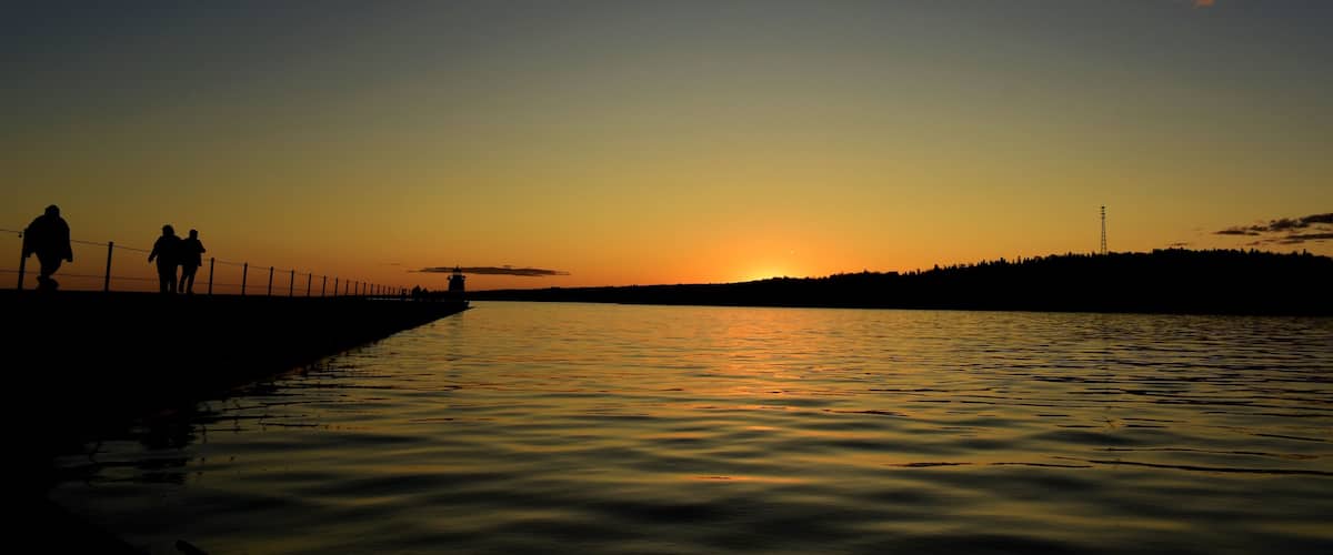 A sunset over a calm body of water with silhouettes of people on a pier.