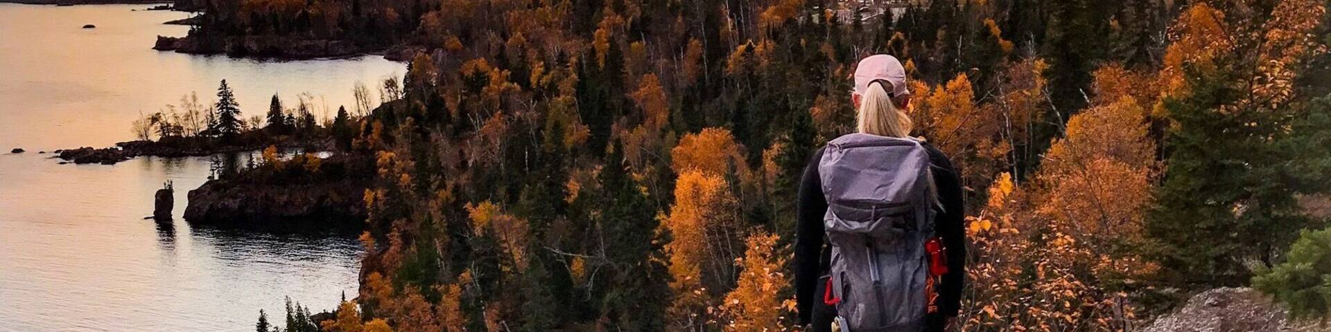 A hiker on a rocky overlook overlooking a lake and forest during sunset.