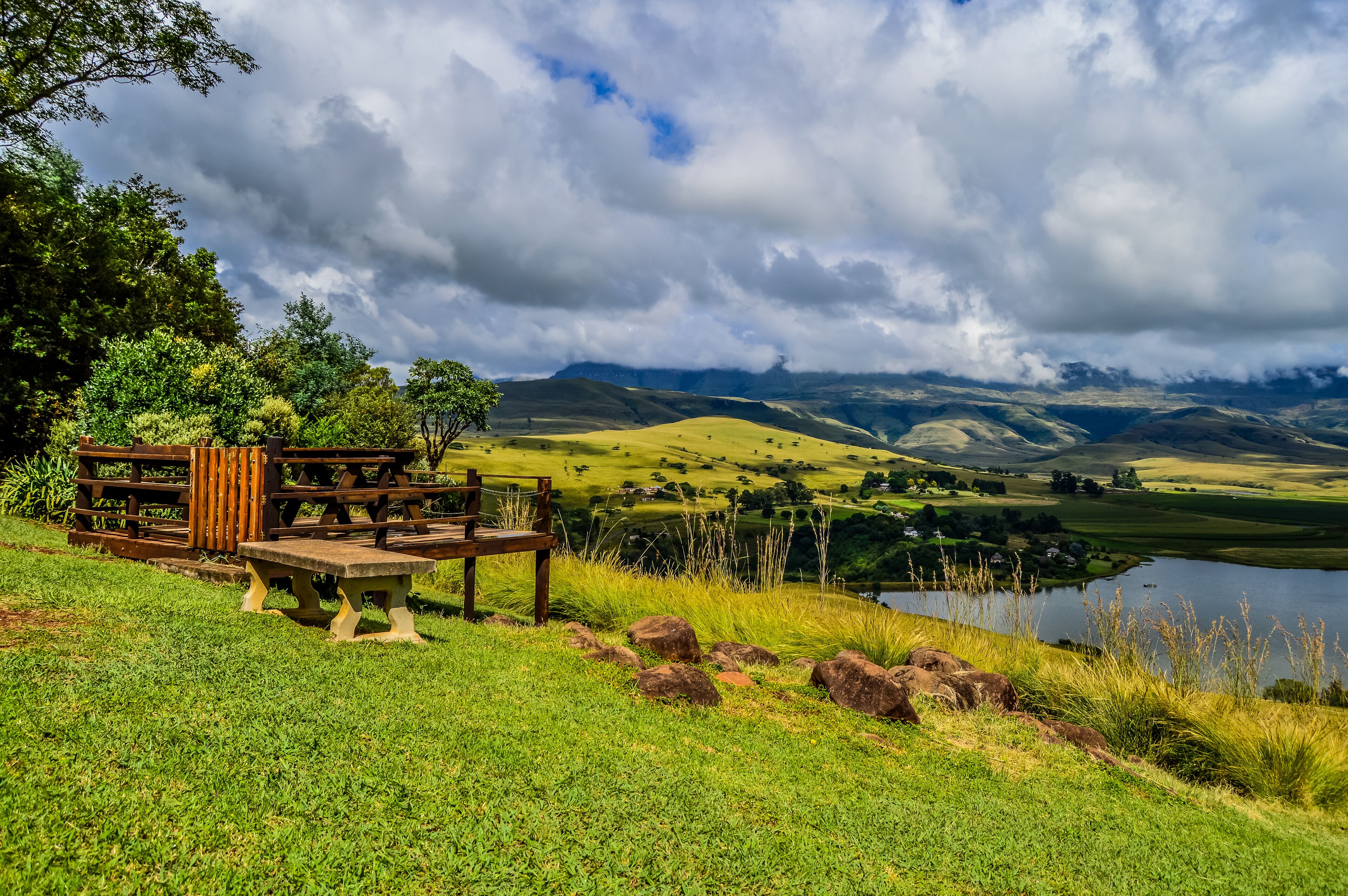 A picnic area with a bench and table overlooking a lake and rolling hills.