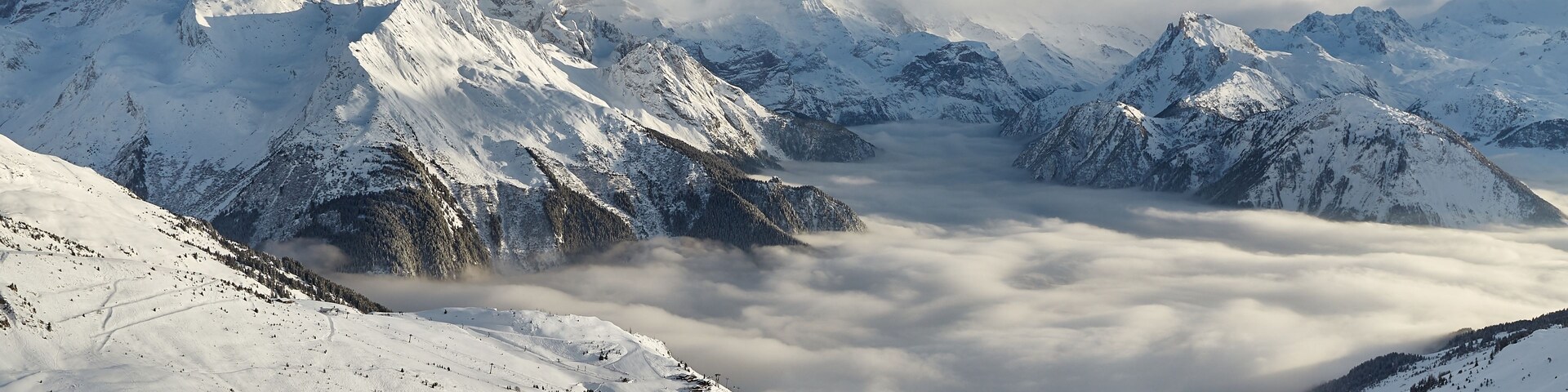 Una cordillera nevada con un valle de nubes abajo.