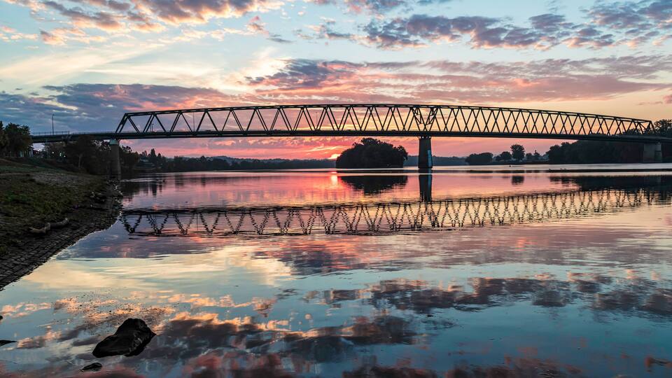 A sunset over a calm river with a bridge and a small island in the distance.