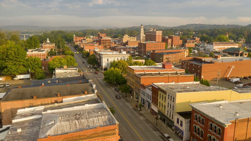 A historic downtown area with a mix of brick buildings, a prominent clock tower, and a river in the background.