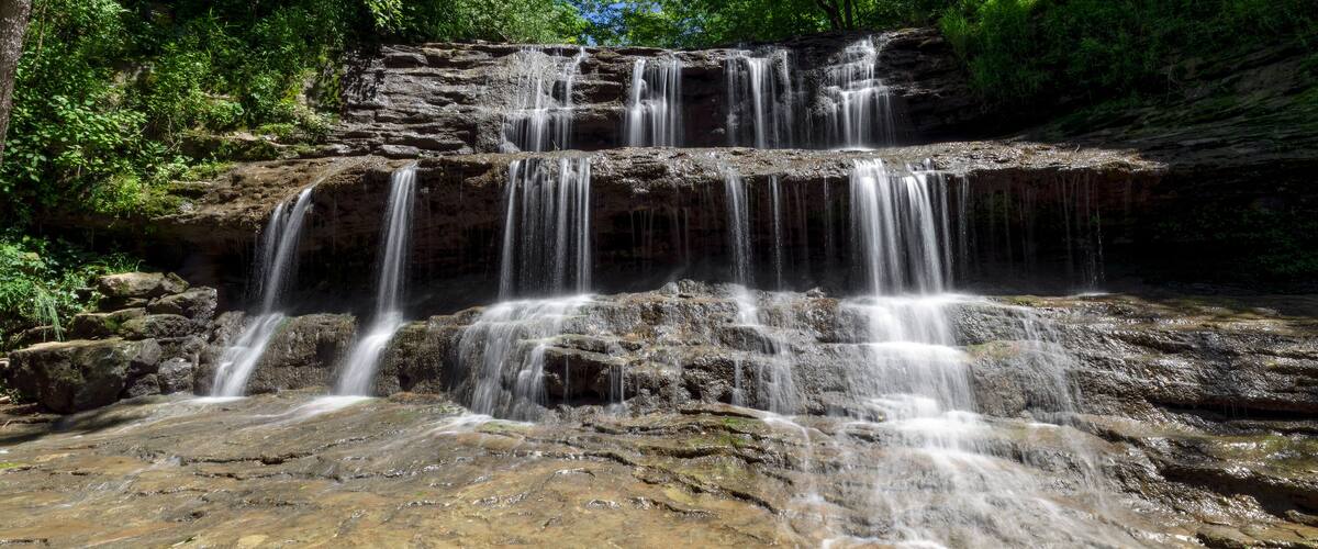 A multi-tiered waterfall surrounded by lush green forest.