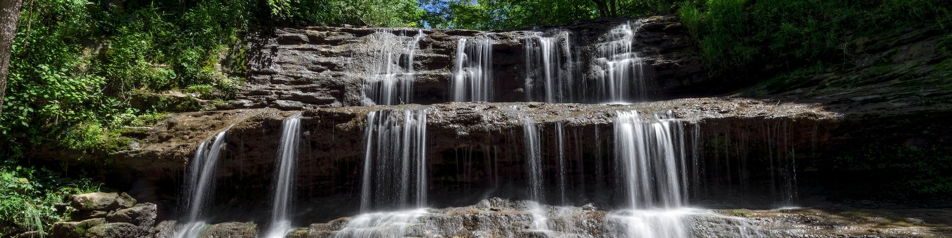 A multi-tiered waterfall surrounded by lush green forest.