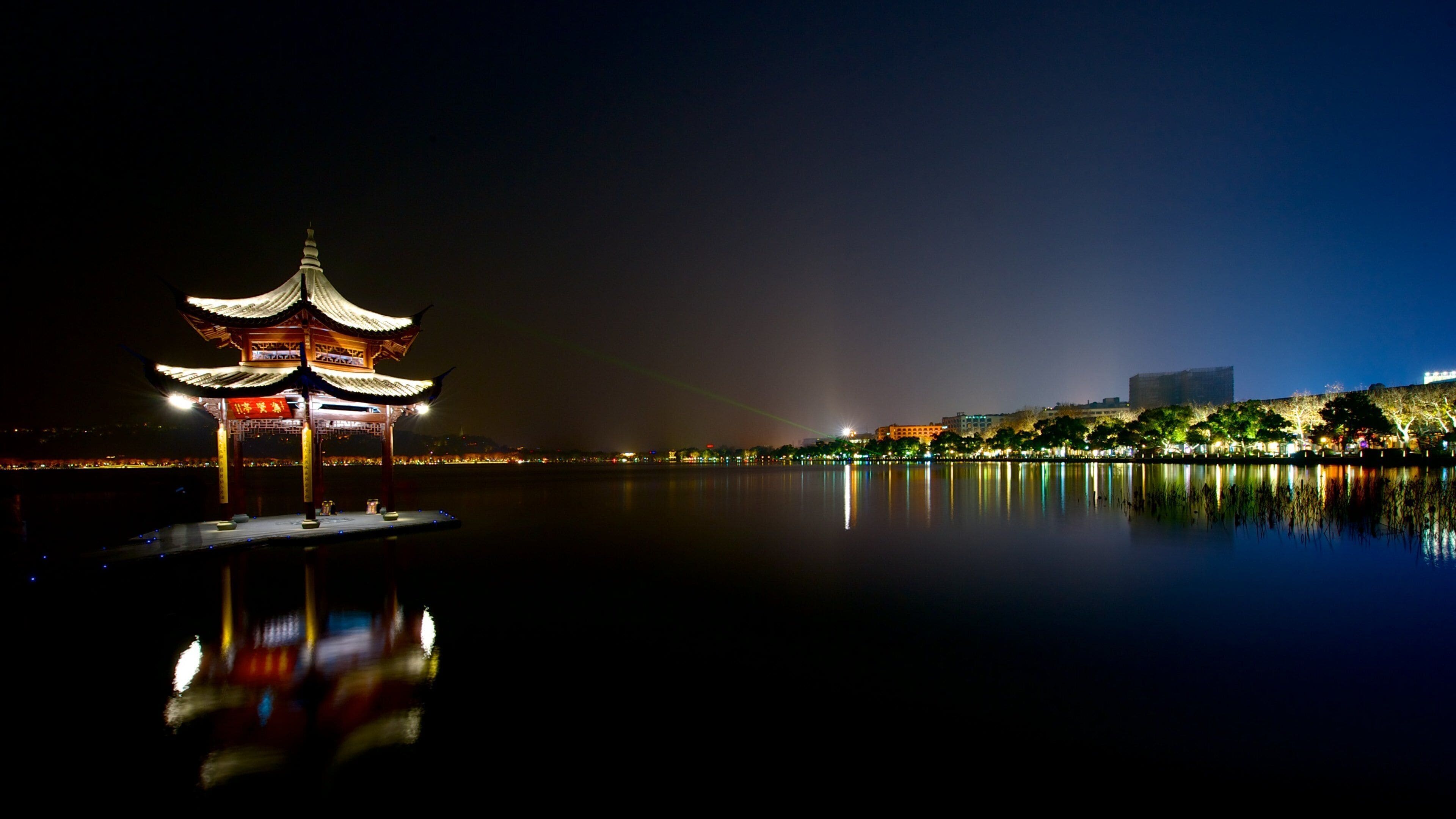 Un pabellón chino tradicional a orillas de un lago tranquilo, reflejando las luces y la arquitectura.