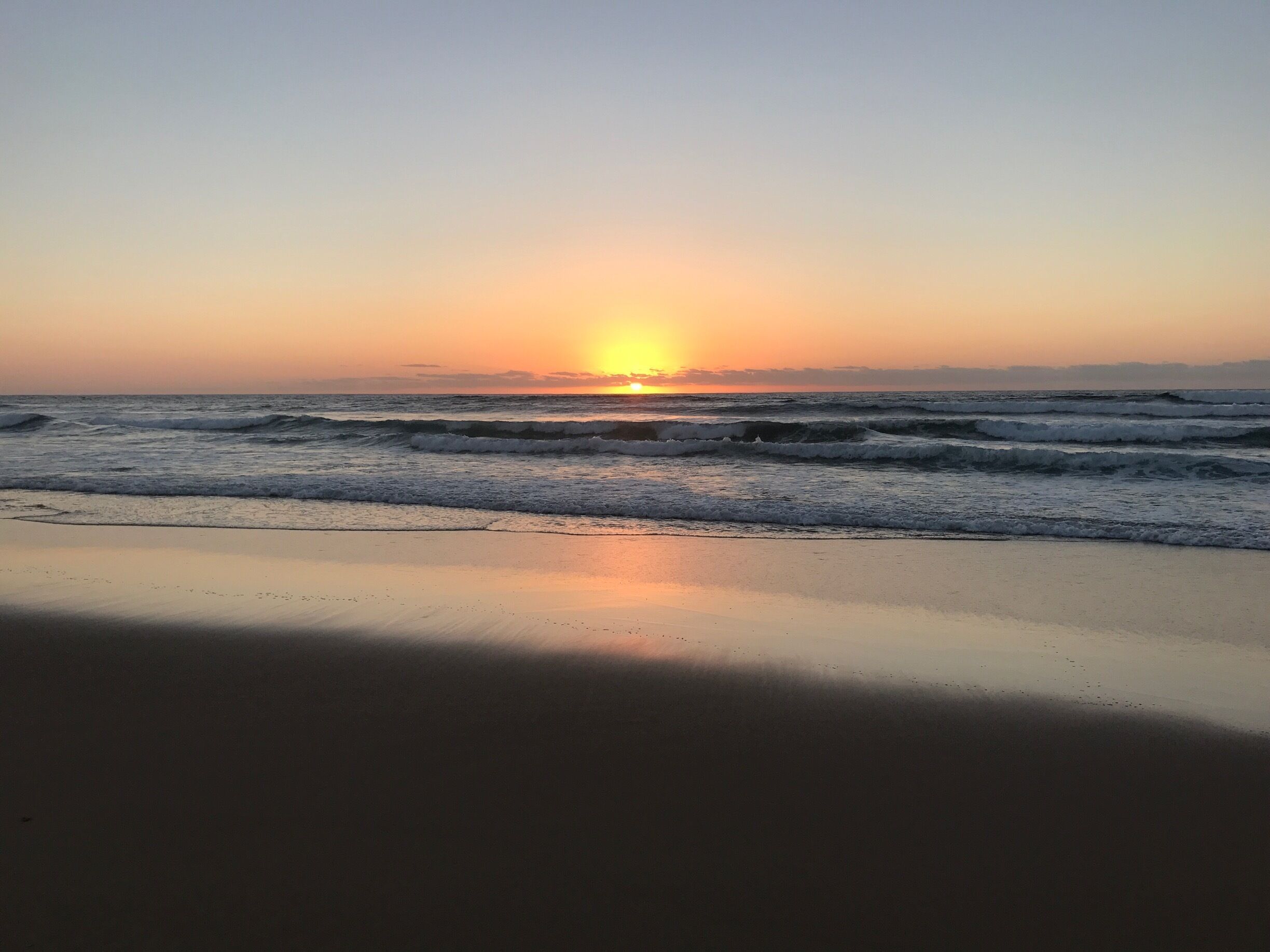 A beach at sunset with waves and a clear sky.