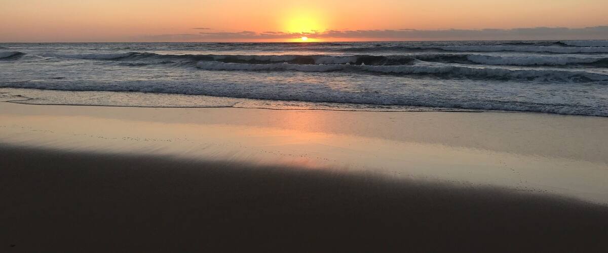 A beach at sunset with waves and a clear sky.